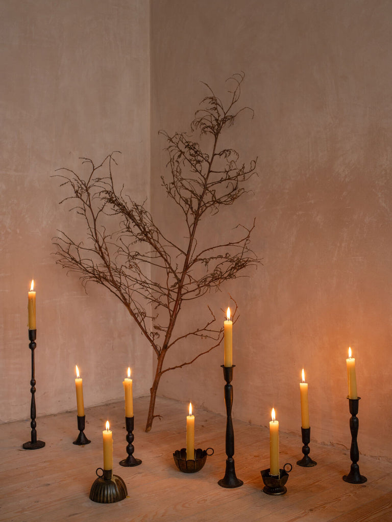 Lit candles in many different styles of black iron candle holders around a festive tree branch