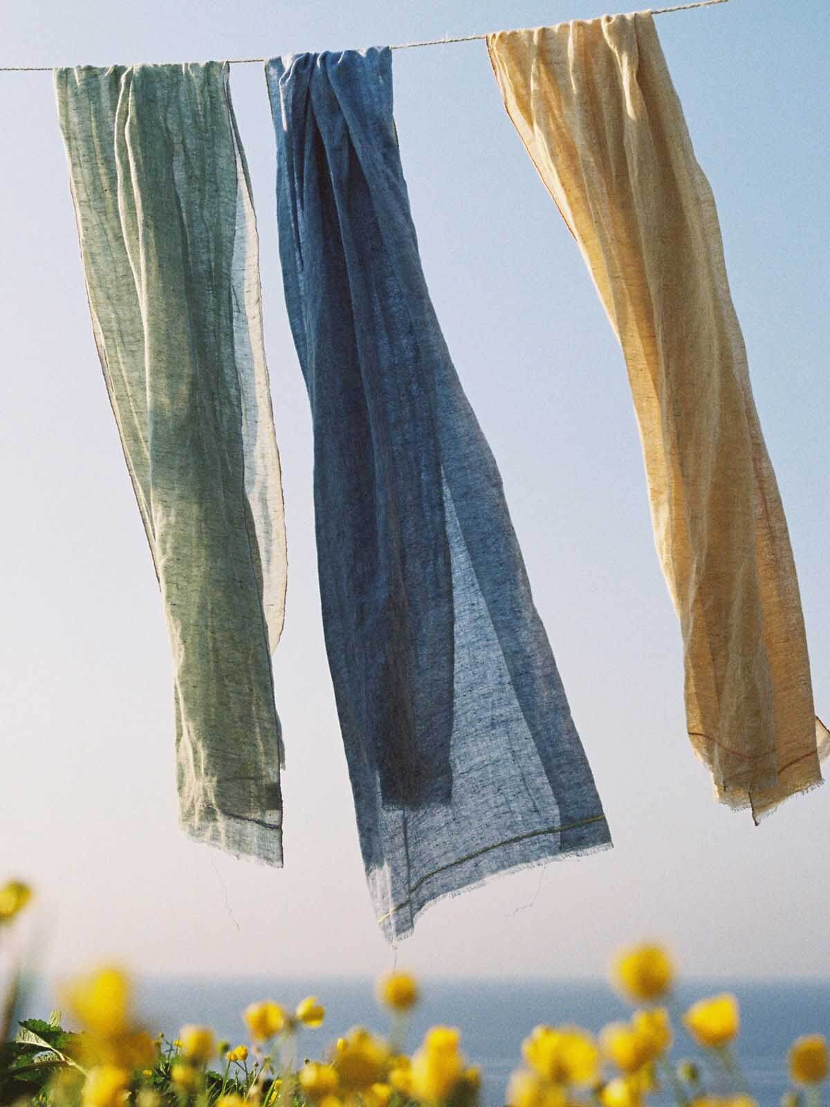 Three Bohemia linen scarves hanging on a washing line above yellow flowers