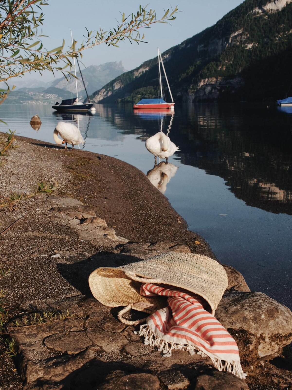 A French style market basket bag with hammam towel on a river bank with swans and boats in the distance