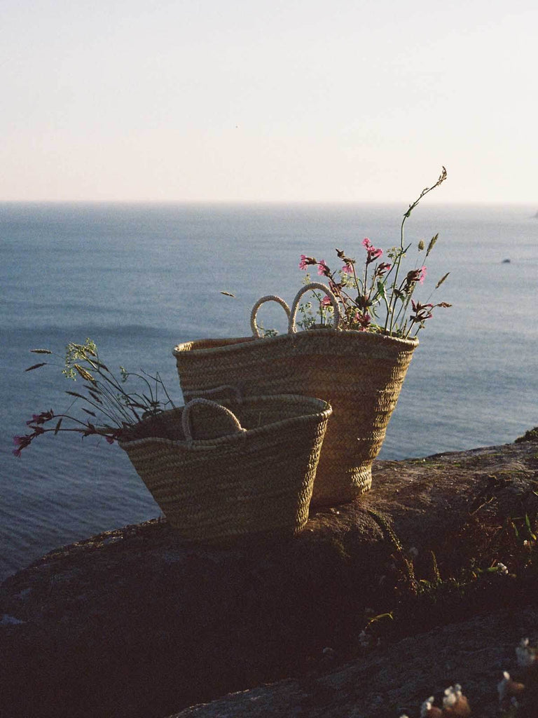 A medium and small Market Basket filled with wildflowers on a clifftop overlooking the blue sea