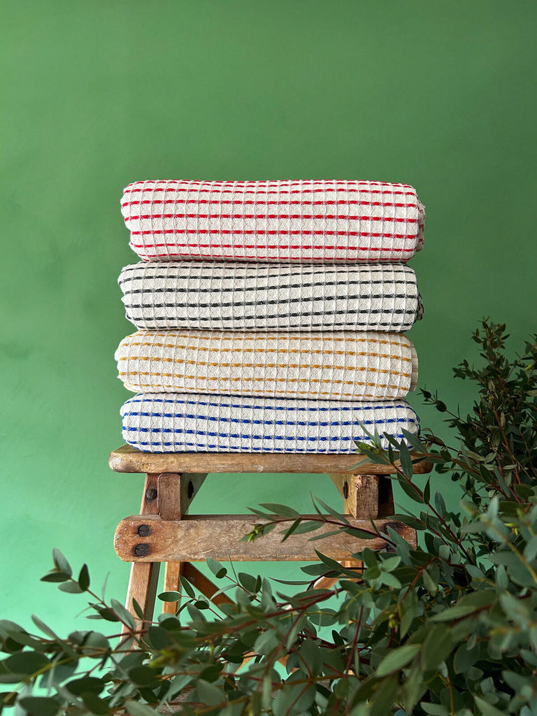 Milos Hammam Towels in four distinct colours folded on a wooden stool