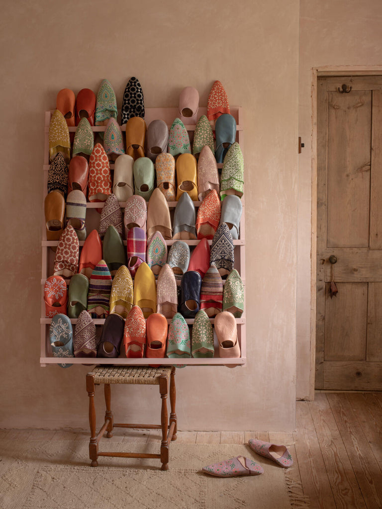 A display of many different Bohemia Moroccan babouche slippers in a rustic plaster pink room.