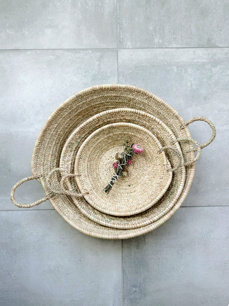 A small, medium and large Moroccan woven plate stacked on a grey tile floor