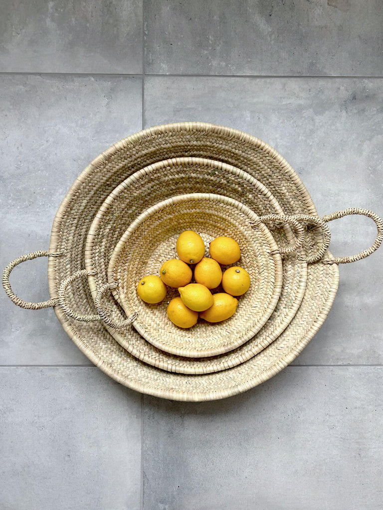 A small medium and large natural woven plate with handles used as a fruit platter with lemons