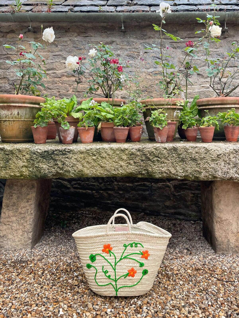 Hand-embroidered whoelsale market basket with a vibrant Nasturtium floral motif, nestled among potted plants | Bohemia Design