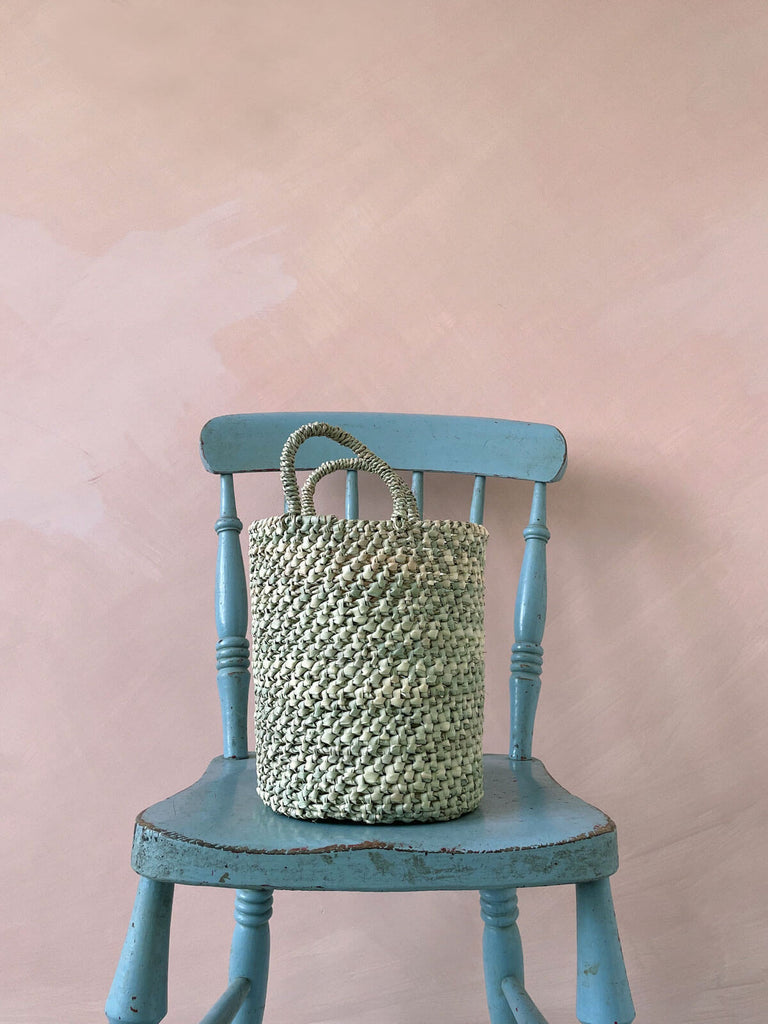 Large round open weave nesting basket with short handles on a blue chair
