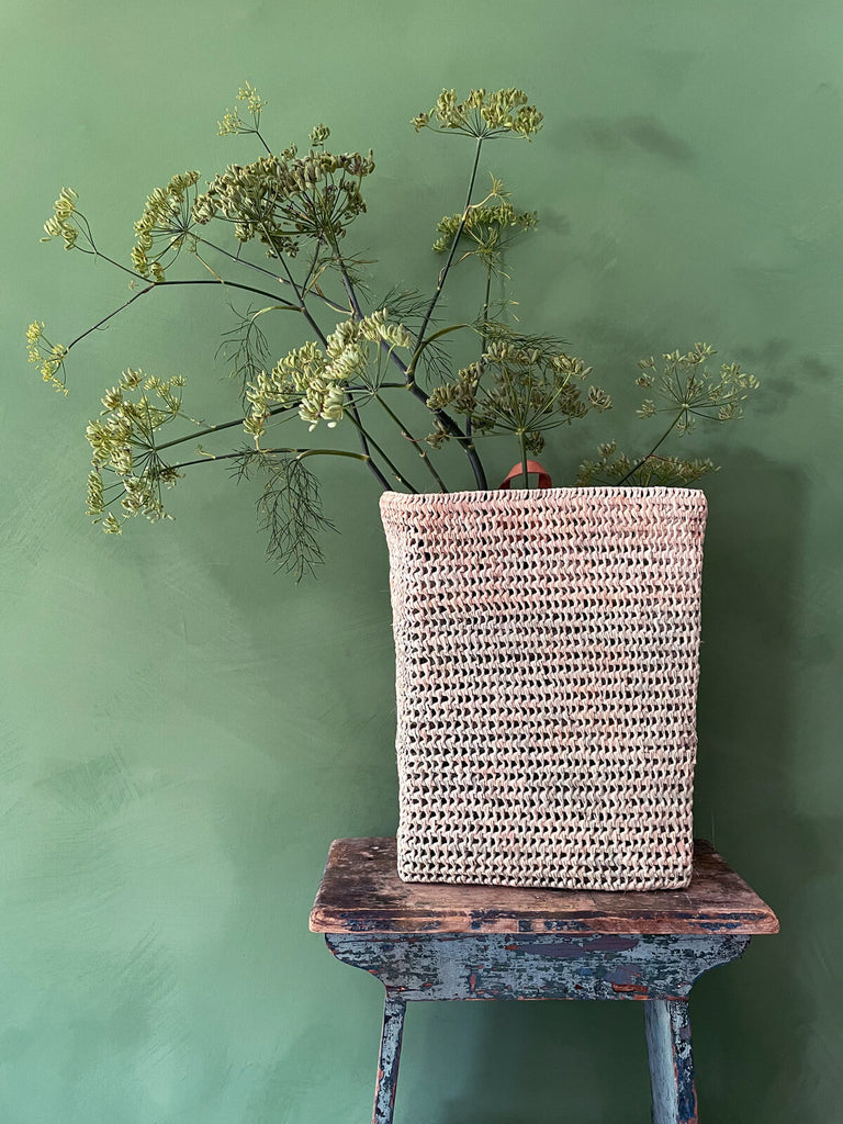 Osaka open weave hanging basket filled with vibrant greenery, resting on a rustic wooden stool | Bohemia Design