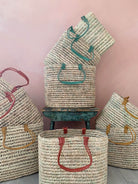 Oval shaped baskets with pleated leather handles in different colours in front of a pink wall