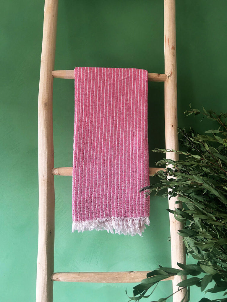 Available for wholesale, a Flamingo pink hammam towel with subtle white stripes displayed on a rustic wooden ladder by Bohemia Design