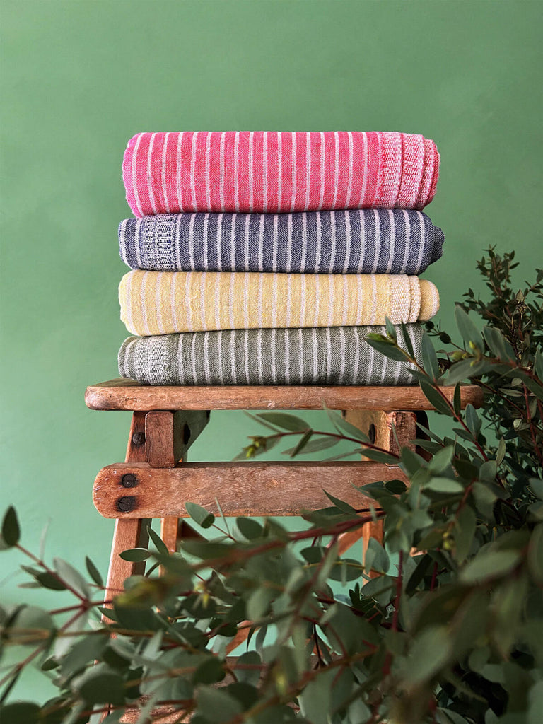 Wholesale Portobello hammam towels in bright stripe design folded on a rustic wooden stool | Bohemia Design