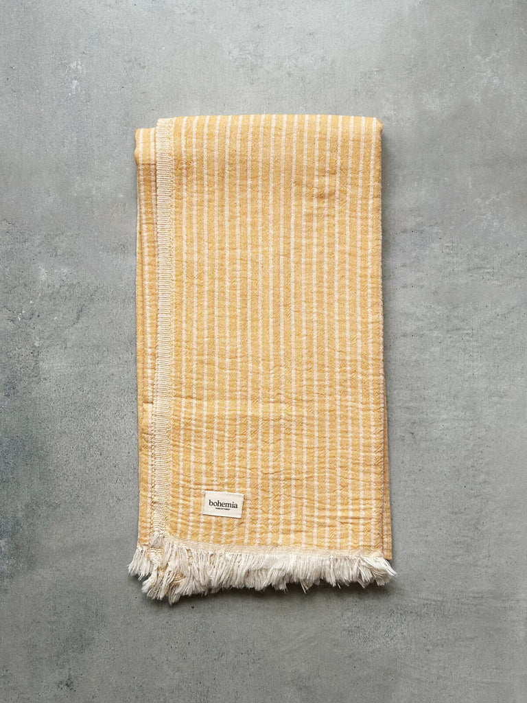 Wholesale Turkish cotton hammam towel in mustard yellow with subtle woven stripes, set against a textured grey background | Bohemia Design