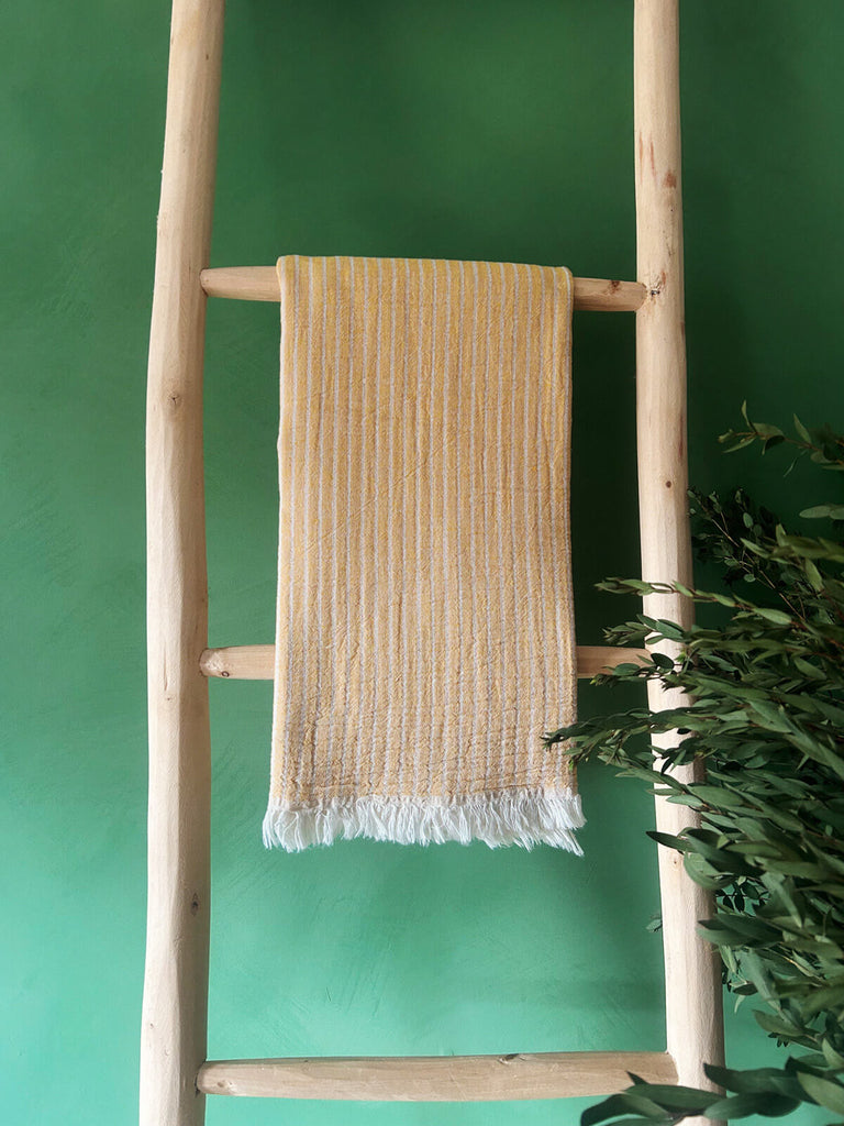 Wholesale mustard-tone hammam towel with subtle stripes, presented on a rustic wooden ladder | Bohemia Design