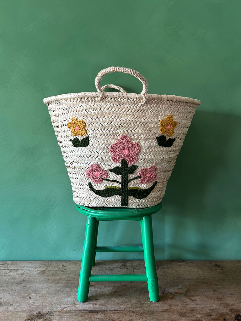 Hand embroidered market basket with two short handles featuring our posy floral design, set against a vibrant green wall by Bohemia