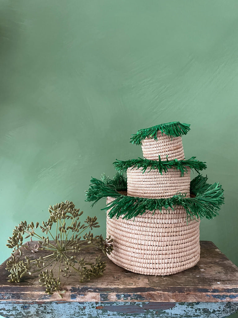 A stack of three green raffia tassel pots on a rustic table against green wall | Bohemia Design 