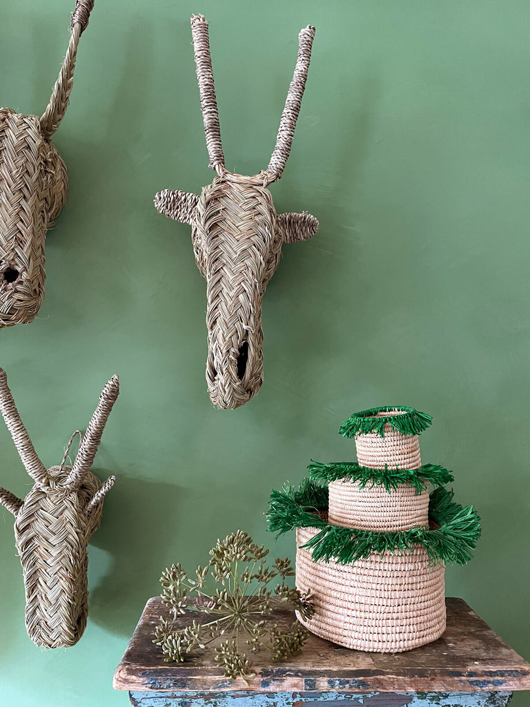 A stack of three green raffia tassel pots with woven animal heads displayed against a green wall | Bohemia Design