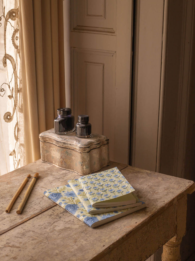 Group of sage cotton paper notebooks with floral block print covers on an antique desk