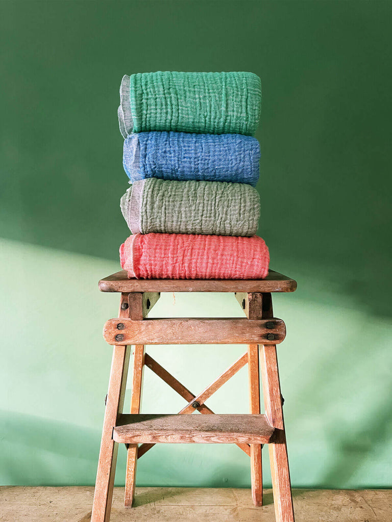 Four Samos hammam towels in different colours folded on a wooden stool