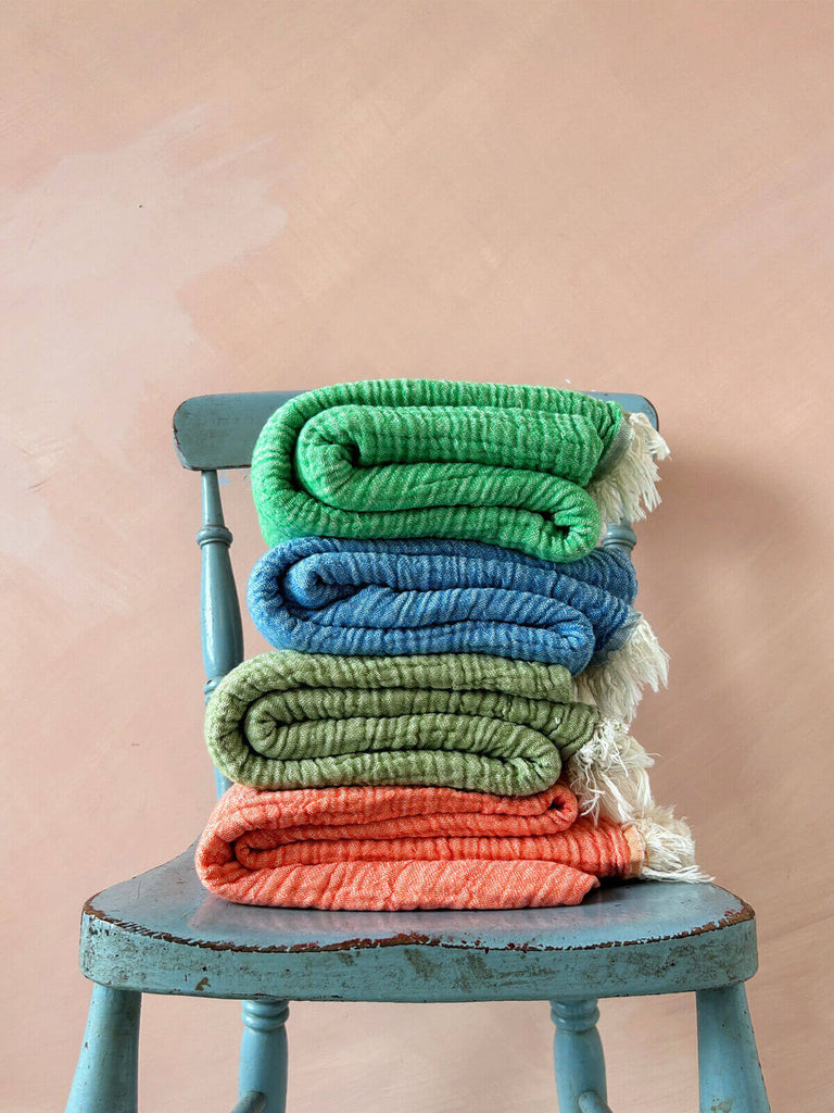 Four folded cotton Samos hammam towels on a blue wooden chair