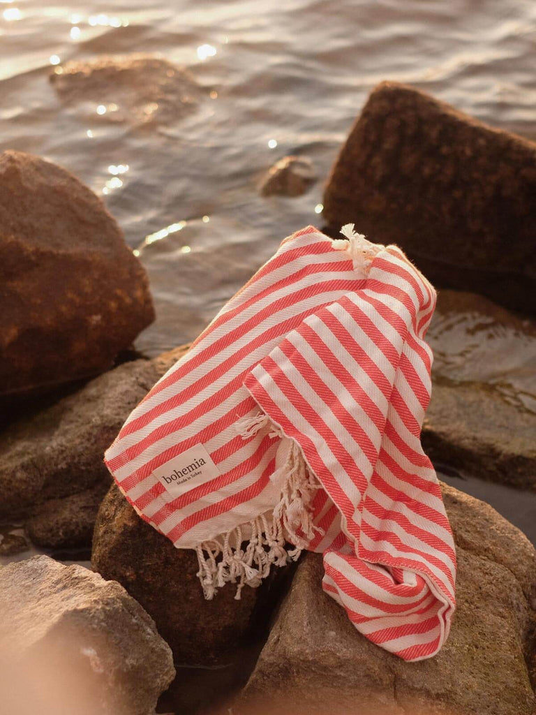 Classic orange and white stripe Sorrento hammam towel on a rocky shoreline
