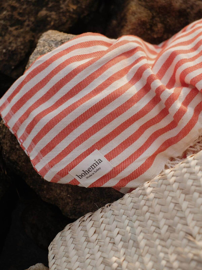 Sorrento hammam towel in orange stripe on some rocks with a Bohemia basket bag