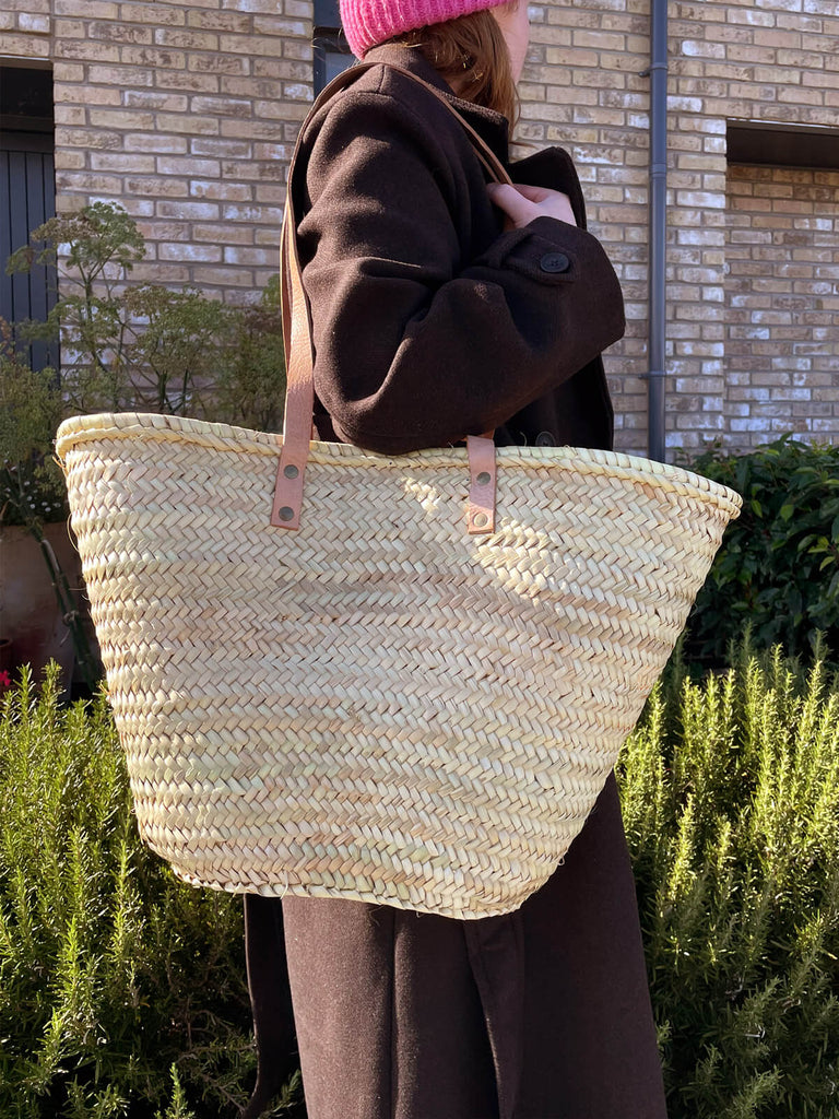 A girl with a large straw shopper bag on her shoulder, standing against a backdrop of greenery and autumn colours | BohemiaDesign