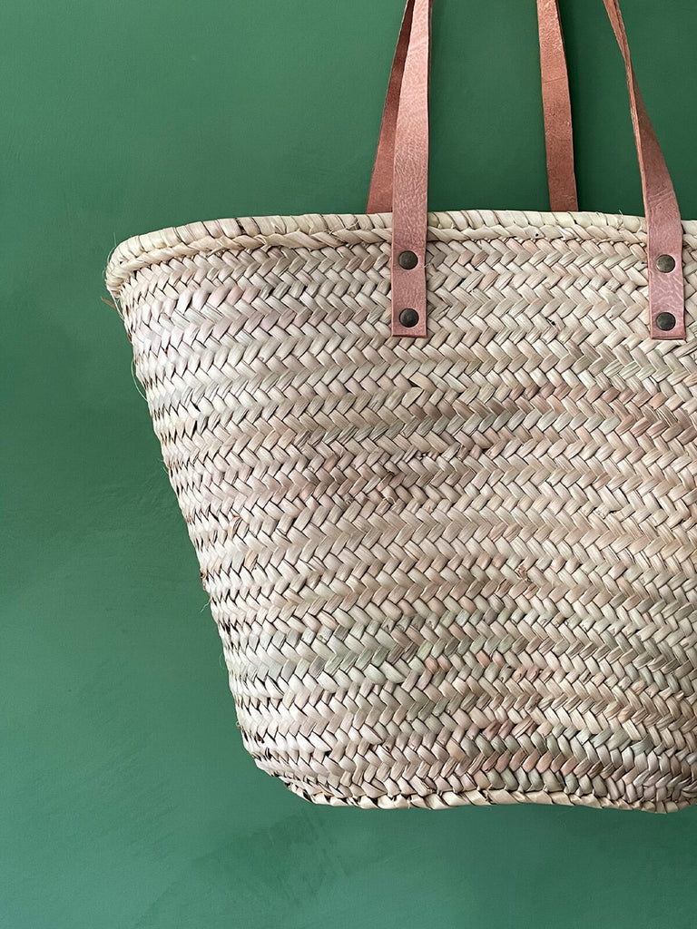 A close-up of a handwoven natural straw basket bag with flat leather shoulder straps | BohemiaDesign