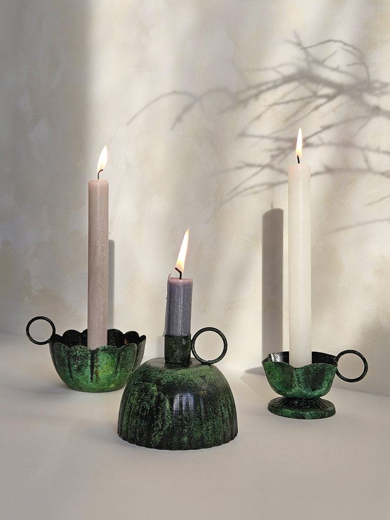 A group of iron candle holders with a vintage moss patina finish with lit candles casting soft shadows on a slightly textured background | Bohemia