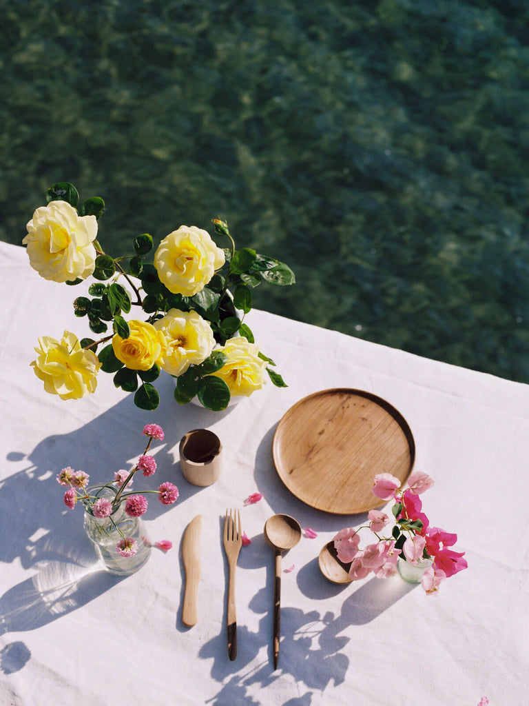 Walnut Wood Plate and other handcrafted wood cutlery on a table with yellow roses by the sea