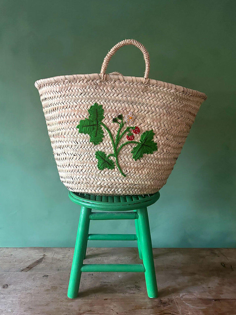 A handcrafted palm leaf market basket featuring a charming hand-embroidered wild strawberry design by Bohemia Design Wholesale