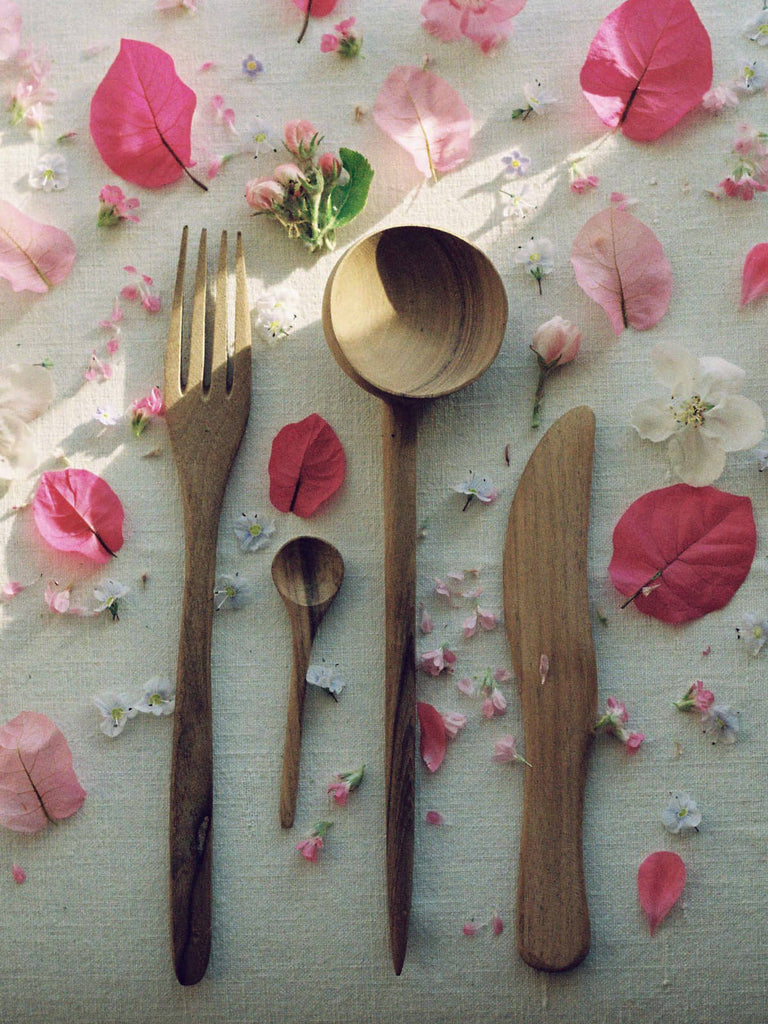 Handcrafted wooden cutlery on a linen tablecloth with pink petals