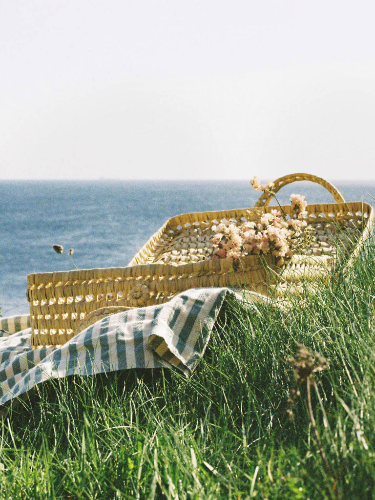 Woven suitcase on a picnic blanket by the coast