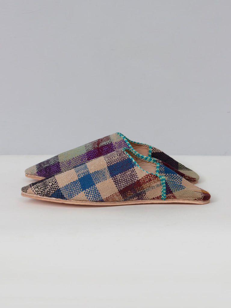 Side view of a pair of limited edition textile and leather Moroccan boujad pointed babouche slippers with a natural check pattern.