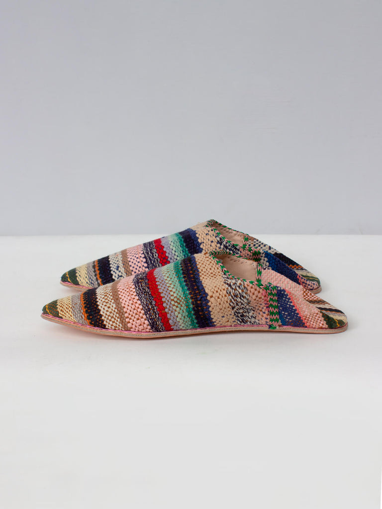 Side view of a pair of limited edition Moroccan boujad fabric and leather pointed babouche slippers with a pastel stripe pattern. 