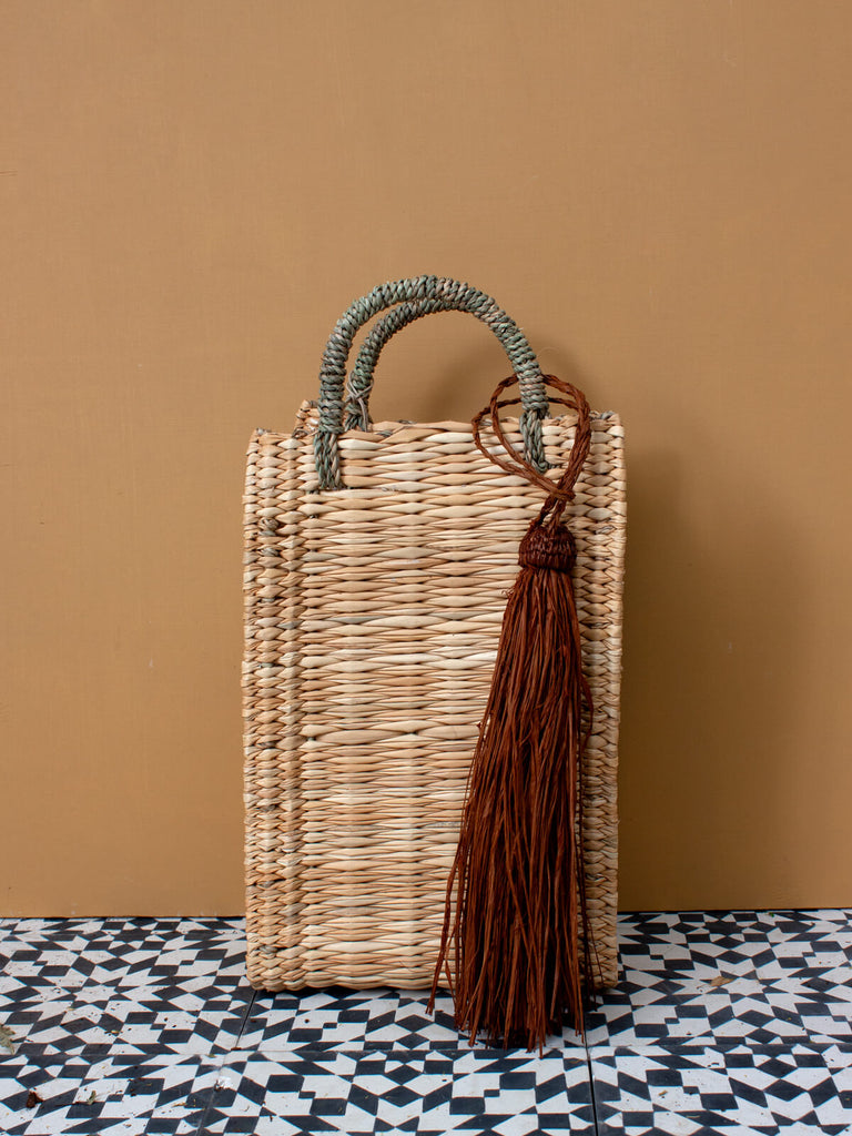 A tobacco brown raffia tassel on a Moroccan reed basket sitting on black and white geometric tiles.