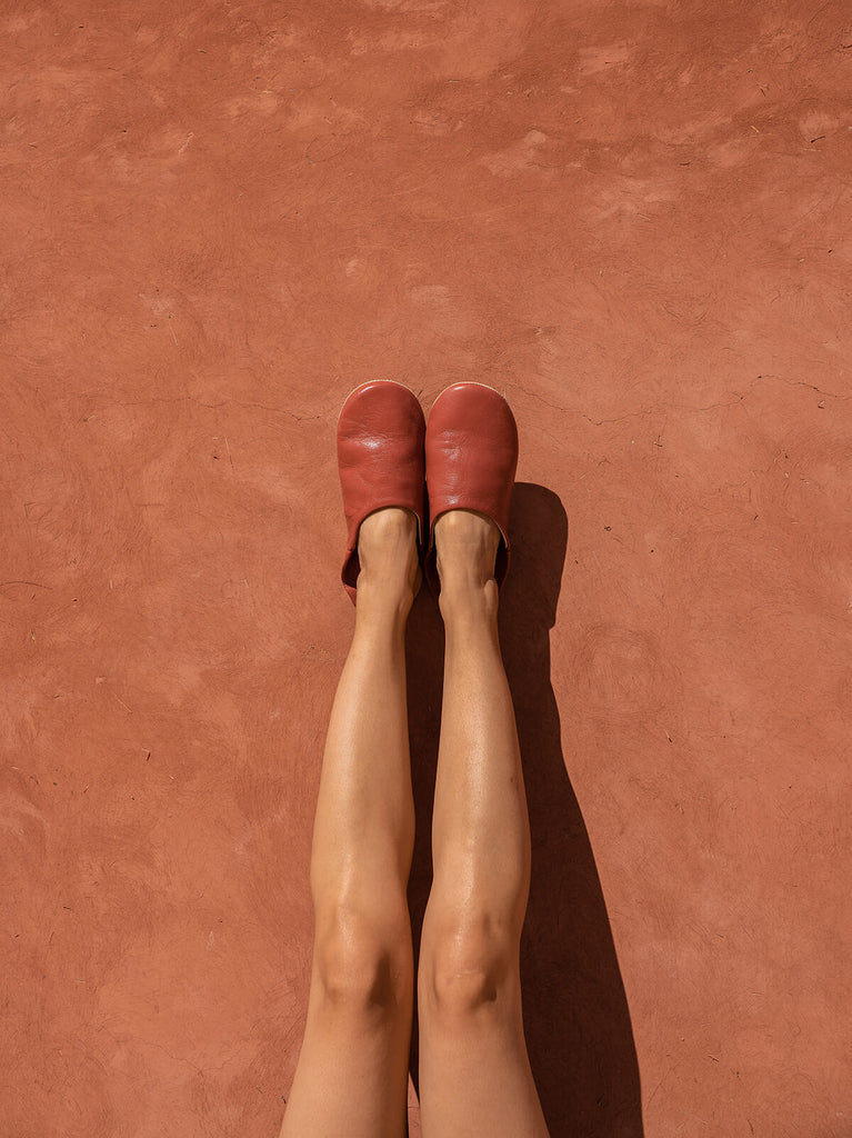 Woman wearing Terracotta Moroccan babouche leather slippers by Bohemia Design against a terracotta wall