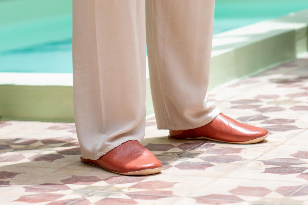 Mens Moroccan babouche slippers in terracotta leather worn by model beside an outdoor pool