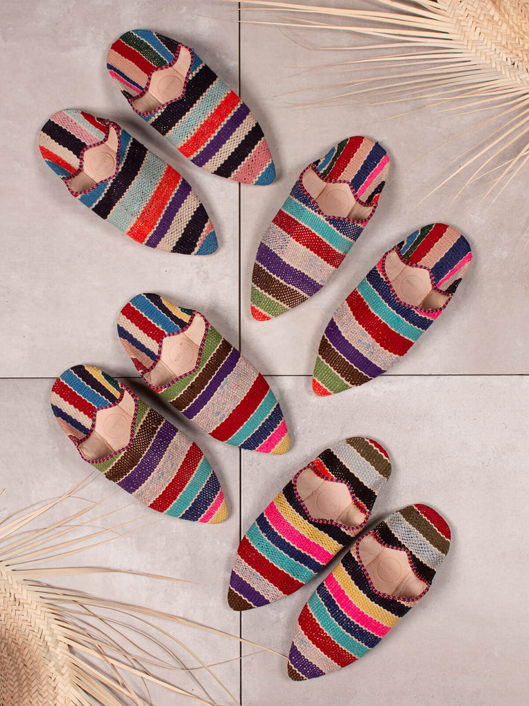 Group of Bohemia design Moroccan babouche boujad slippers in a multi stripe pattern against grey tiles and raffia baskets