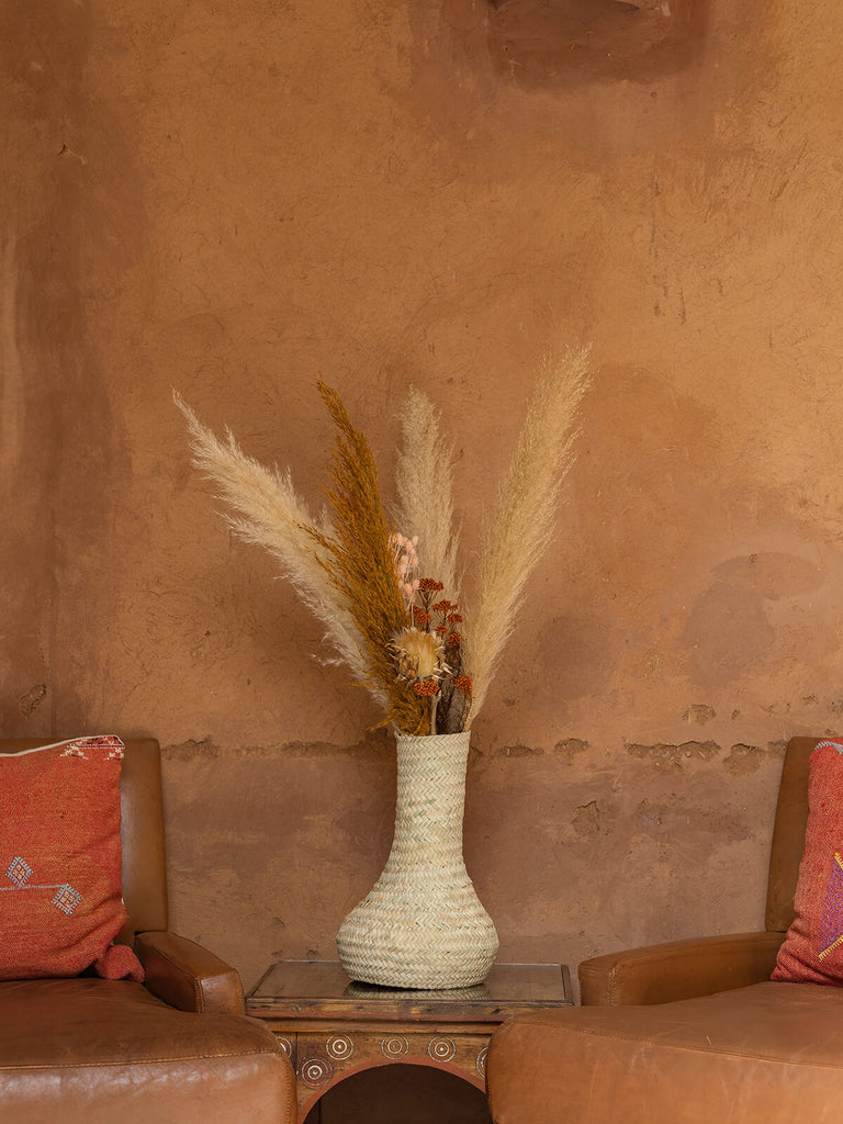 Bohemia design palm leaf basket vase on a wooden table with two chairs against a terracotta wall