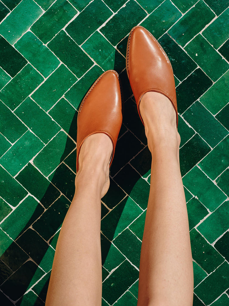 Woman wearing Leather tan mules by Bohemia Design against green tiles