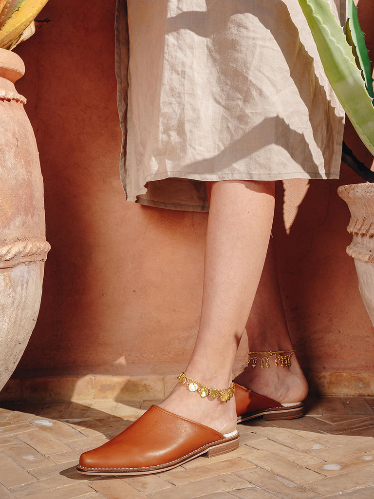 Woman wearing slip on leather tan mules by Bohemia Design with gold anklets