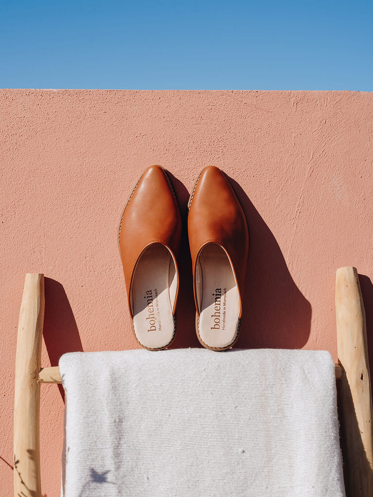Leather tan mules by Bohemia Design against a terracotta wall on a wooden ladder