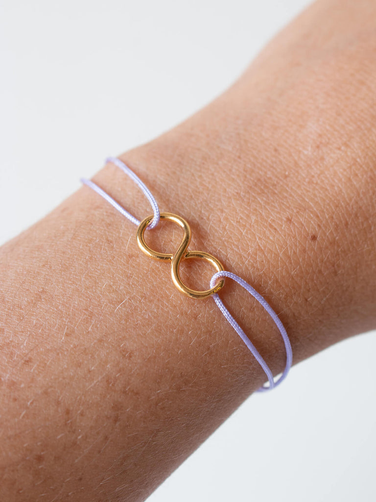 Woman wearing gold infinity bracelet with lilac silk thread by Bohemia Design