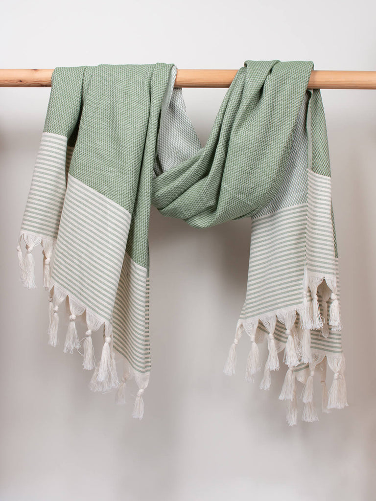 Striped Amalfi Hammam Towel in olive stripe by Bohemia Design hanging on a wooden rod