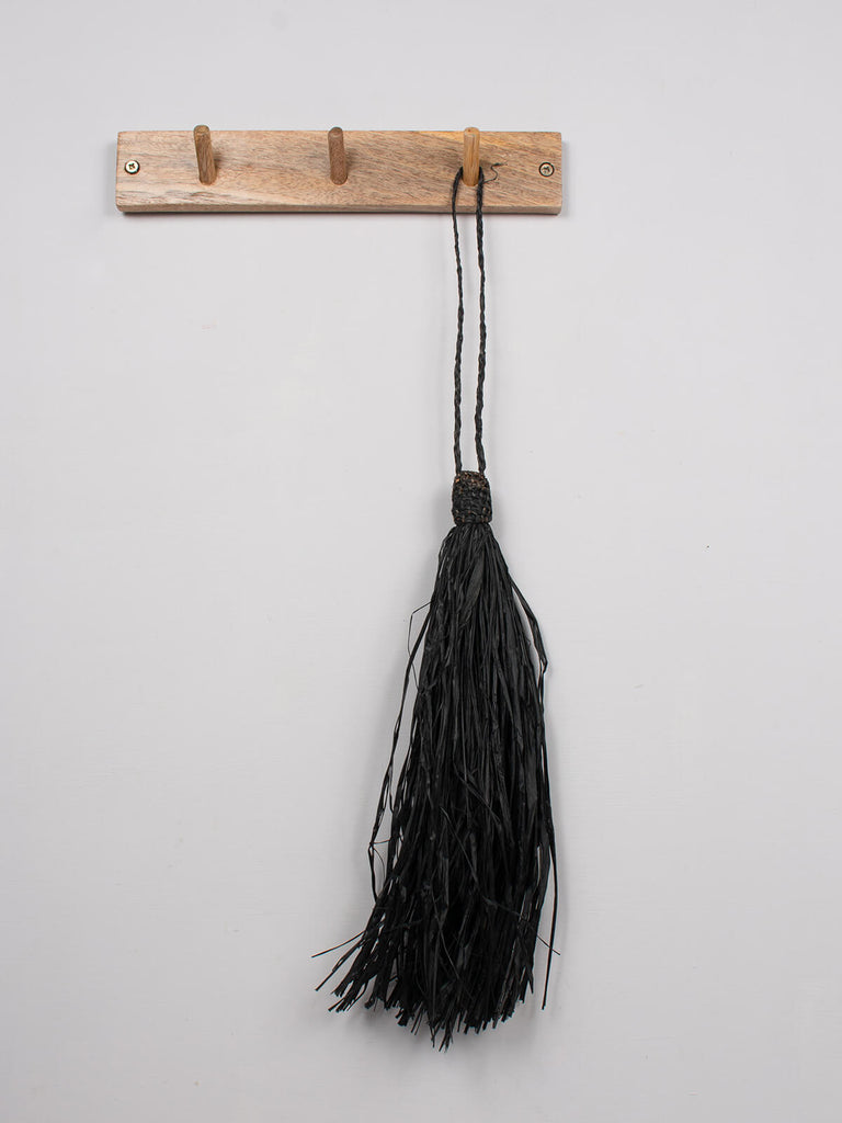 Black raffia tassel hanging on a wooden hook