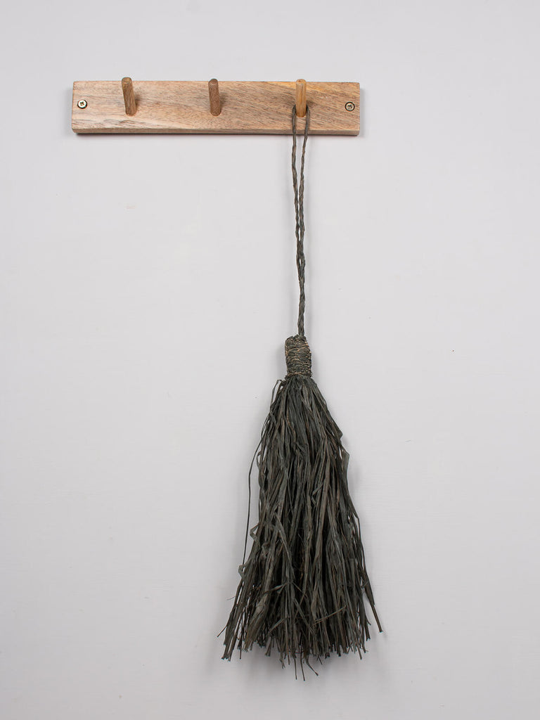 Charcoal raffia tassel hanging on a wooden hook