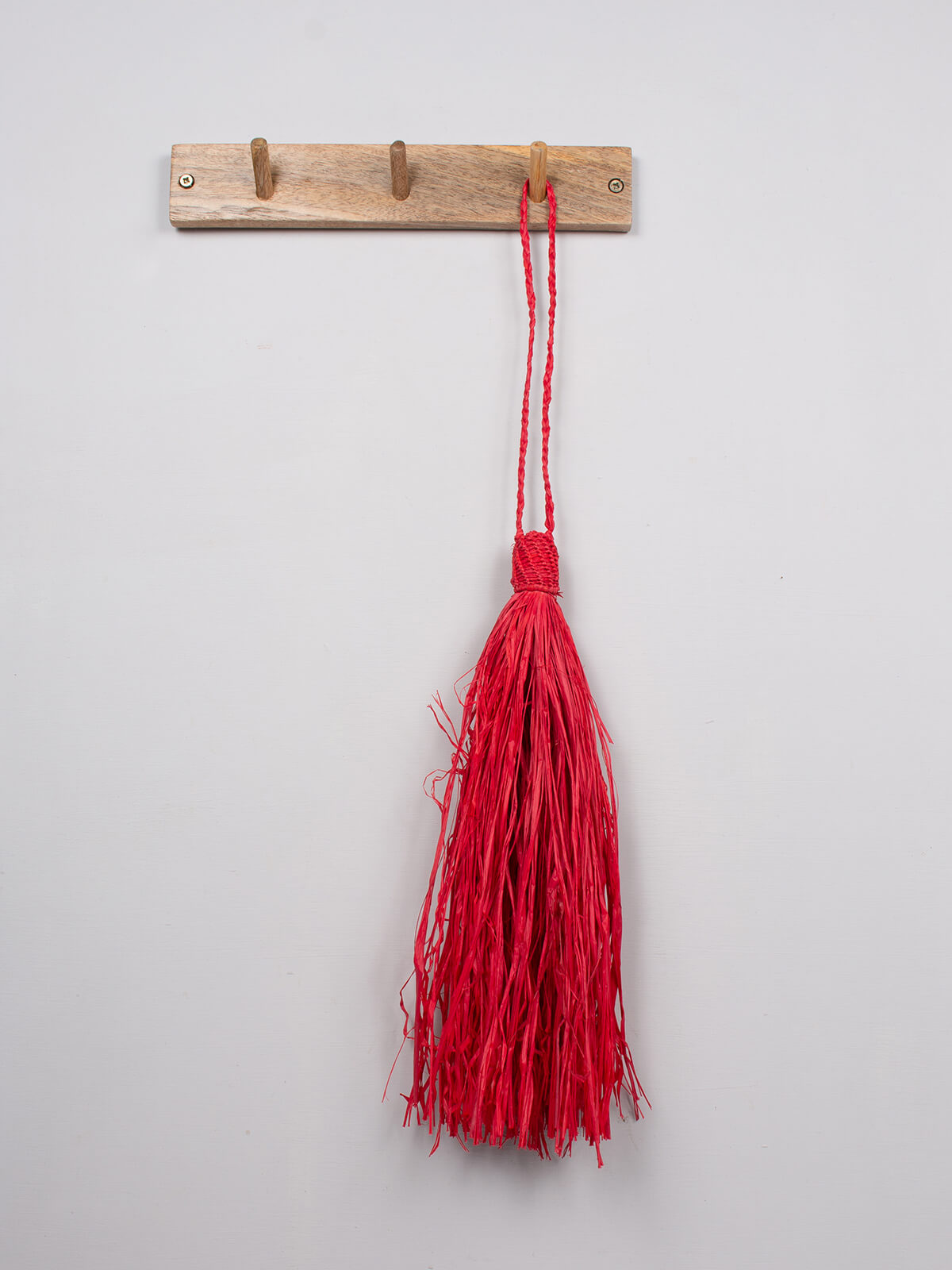 Red raffia tassel hanging on a wooden hook